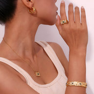 Bracelet jonc doré en acier inoxydable avec détails verts et symboles, porté au poignet féminin.