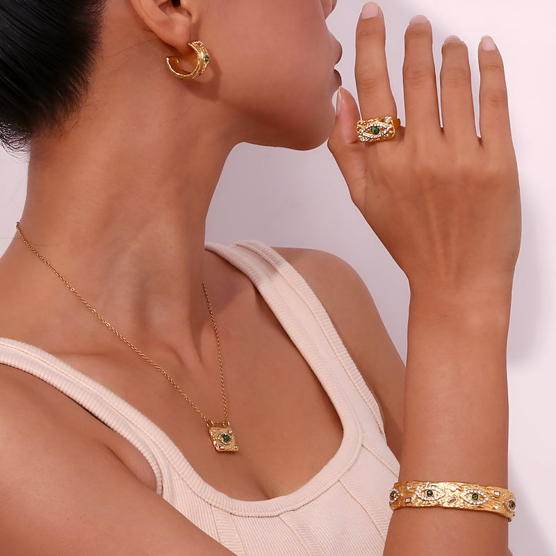 Bracelet jonc doré en acier inoxydable avec détails verts et symboles, porté au poignet féminin.