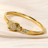 Bracelet jonc en or avec tête de léopard ornée de cristaux et yeux verts étincelants.