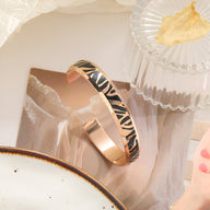 Bracelet jonc en titane or rosé avec motif tigré noir et doré, finition brillante, design épuré et moderne.