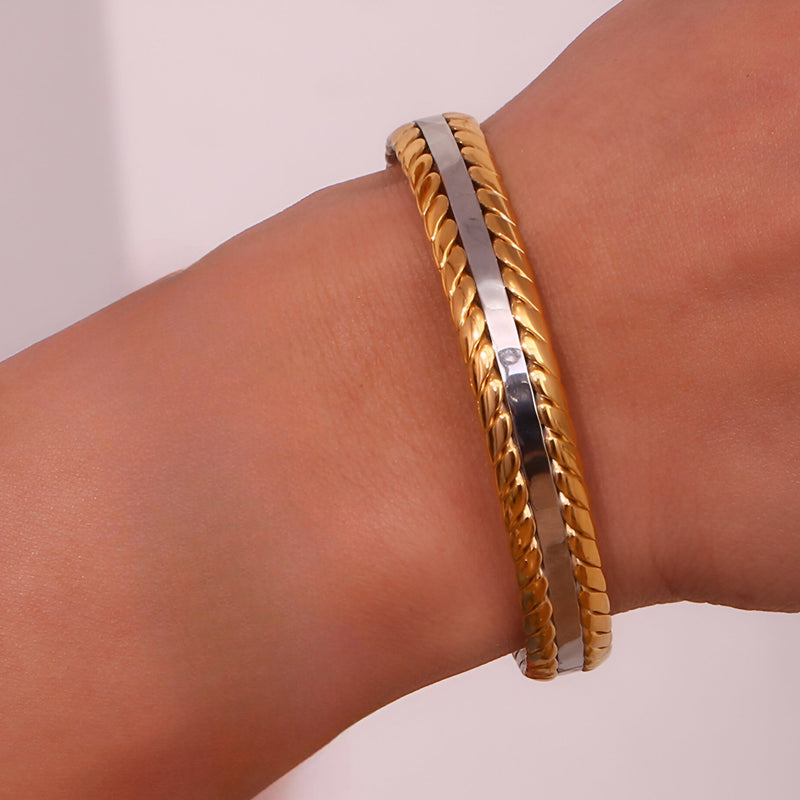 Bracelet jonc fin en acier inoxydable plaqué or et argent, tressage délicat sur poignet.