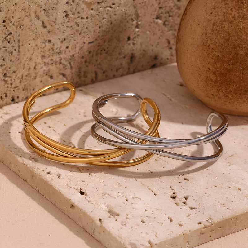 Bracelet jonc torsadé triple en acier inoxydable doré et argenté posé sur pierre naturelle.