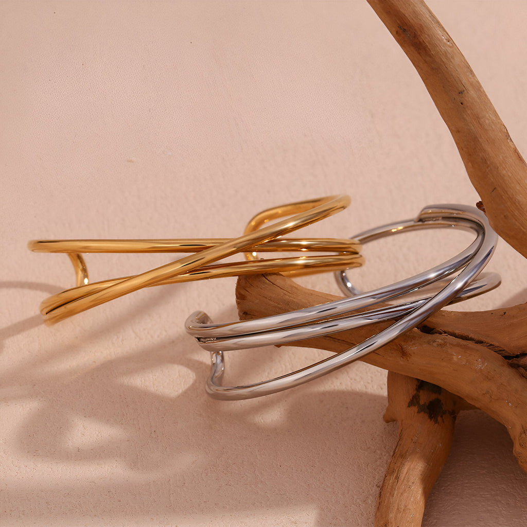 Bracelet jonc duo torsadé en acier inoxydable finition or et argent sur bois naturel.