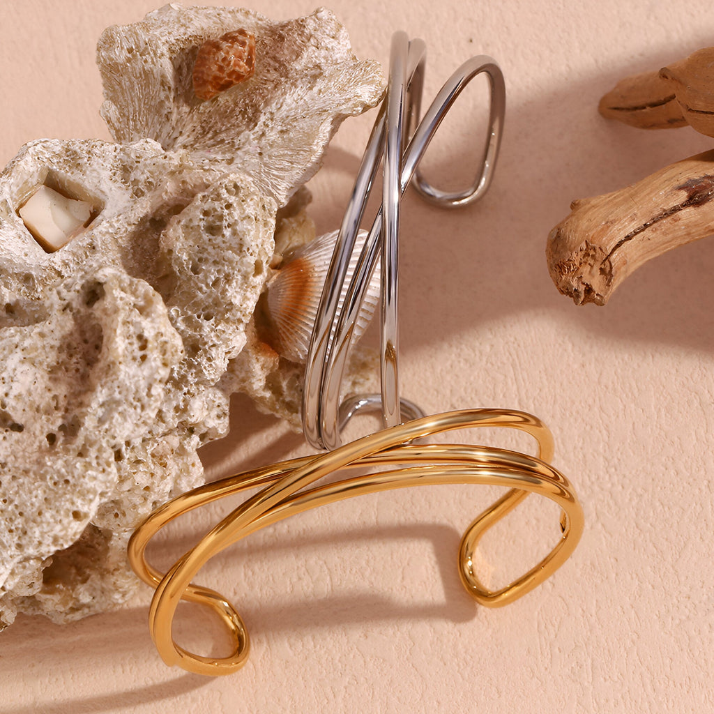 Bracelet jonc trio torsade en acier inoxydable argenté posé sur pierre beige avec bracelet doré devant.