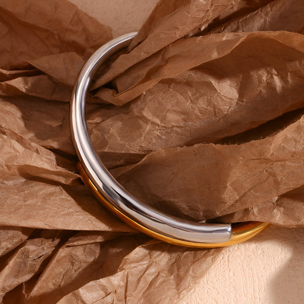 Bracelet jonc bicolore or et argent en acier inoxydable modèle Harmonie posé sur papier froissé marron.