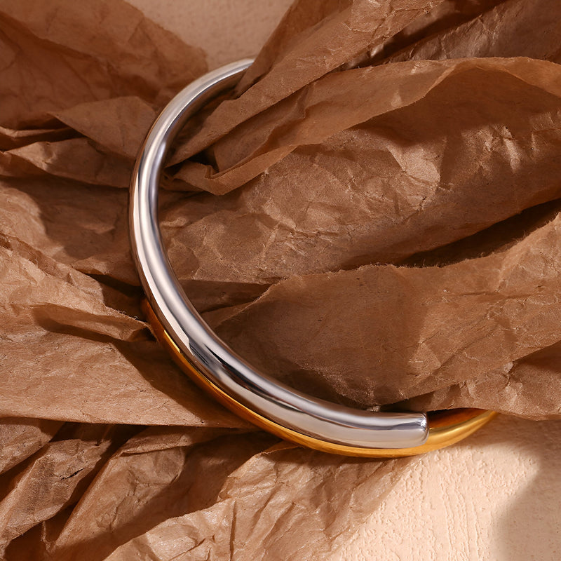 Bracelet jonc bicolore or et argent en acier inoxydable modèle Harmonie posé sur papier froissé marron.