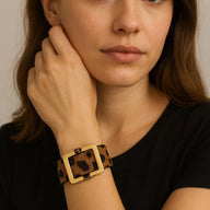 Bracelet large en cuir beige à motif léopard avec boucle carrée dorée porté au poignet.