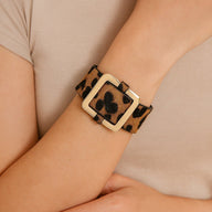 Bracelet large en tissu léopard marron avec boucle carrée beige porté au poignet féminin.