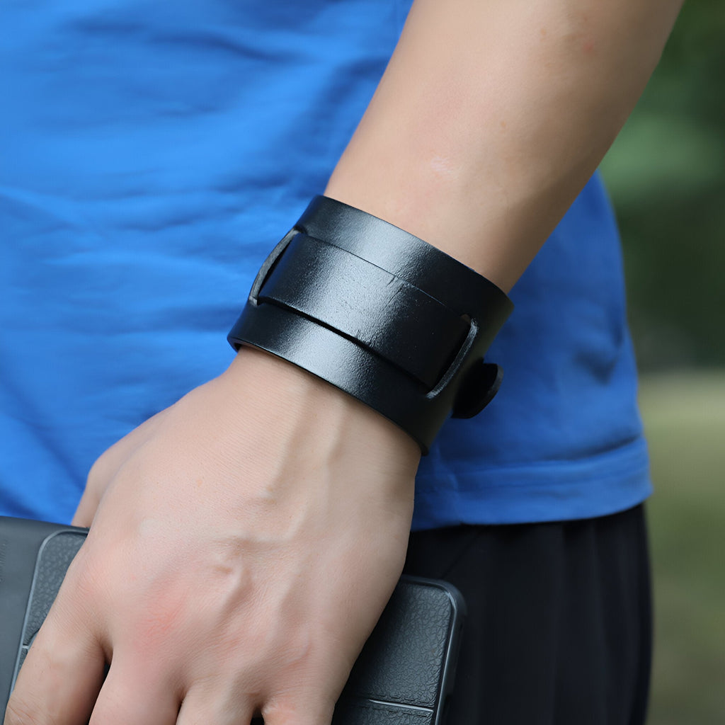 Bracelet large en cuir noir à ardillon, style masculin et moderne, porté au poignet.