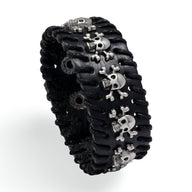 Bracelet large en cuir noir avec plusieurs têtes de mort argentées et couture apparente.