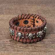 Bracelet large en cuir marron avec multiples têtes de mort en métal argenté et coutures apparentes.