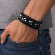 Bracelet large en cuir noir tressé avec multiples têtes de mort métalliques sur poignet masculin.