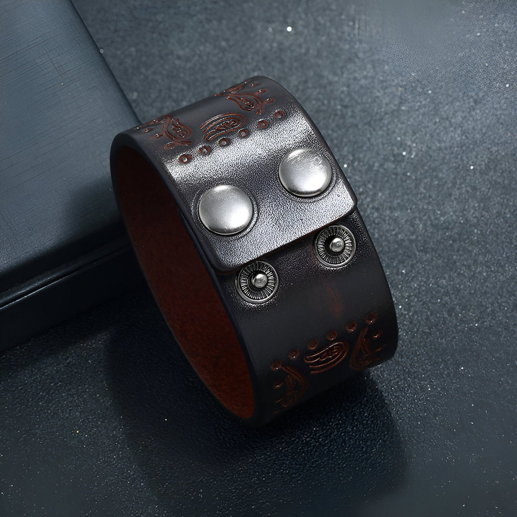 Bracelet large en cuir café avec motifs western gravés et fermoir à boutons pression en métal argenté.