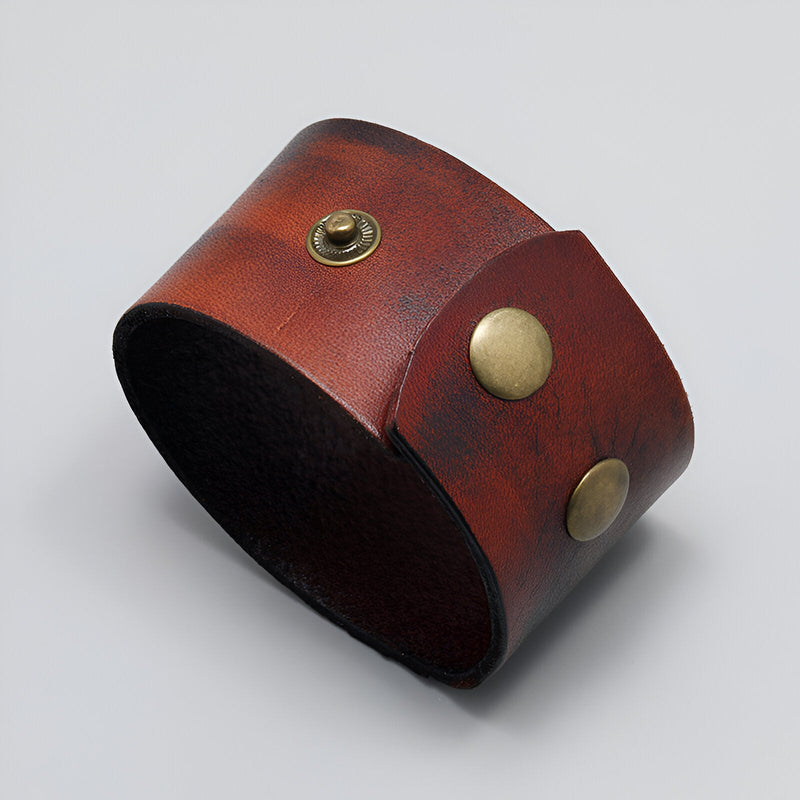 Bracelet large en cuir marron avec fermoirs métalliques dorés et design minimaliste.