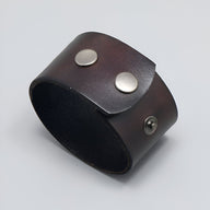 Bracelet large en cuir café avec deux gros boutons métalliques argentés, style minimaliste et mixte.