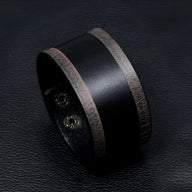 Bracelet large en cuir noir avec bords marron vintage et fermeture à pression métallique.