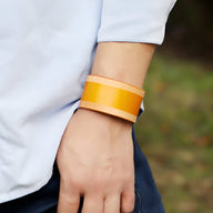 Bracelet large en cuir cognac style rétro avec doublure beige sur poignet masculin.