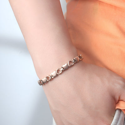 Bracelet magnétique en titane or rosé avec maillons en forme de cœur sur poignet féminin.