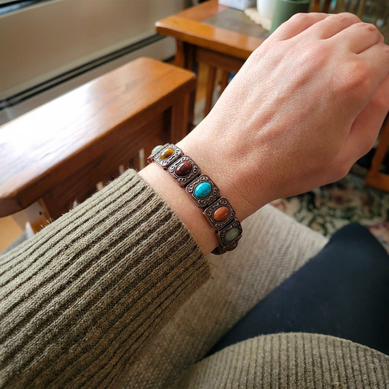 Bracelet en cuivre à larges maillons carrés ornés de pierres naturelles colorées sur poignet.