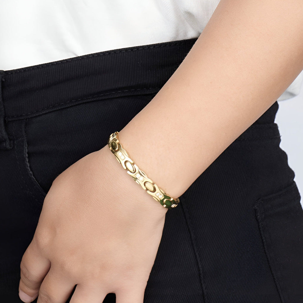 Bracelet magnétique en titane or avec maillons larges et finition brillante porté au poignet femme.