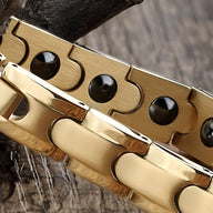 Bracelet magnétique en titane or, avec maillons larges et détails ronds noirs.