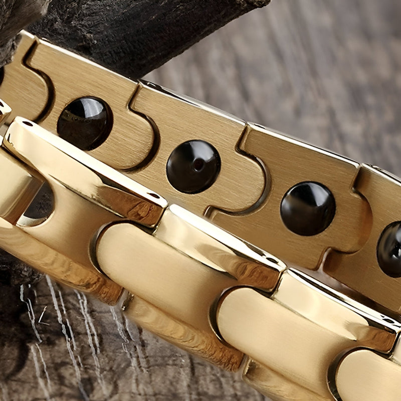 Bracelet magnétique en titane or, avec maillons larges et détails ronds noirs.