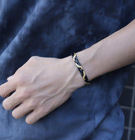 Bracelet magnétique fin en titane noir avec motif camouflage doré, porté au poignet masculin.
