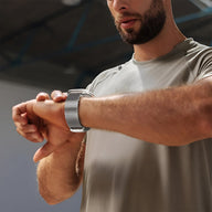 Bracelet maille milanaise acier inoxydable gris avec fermoir tactique porté sur Apple Watch par homme en t-shirt gris.