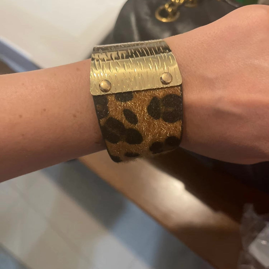 Bracelet manchette large en cuir effet léopard marron avec plaques métalliques dorées rivetées.