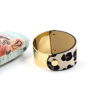 Bracelet manchette doré avec fermeture en tissu à motif léopard noir et beige.
