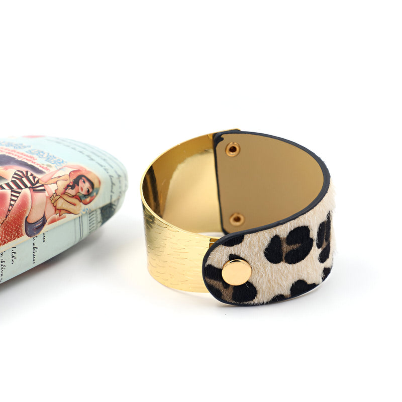Bracelet manchette doré avec fermeture en tissu à motif léopard noir et beige.