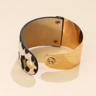 Bracelet manchette doré à effet martelé avec intérieur imprimé léopard beige et marron, fermeture à bouton pression.