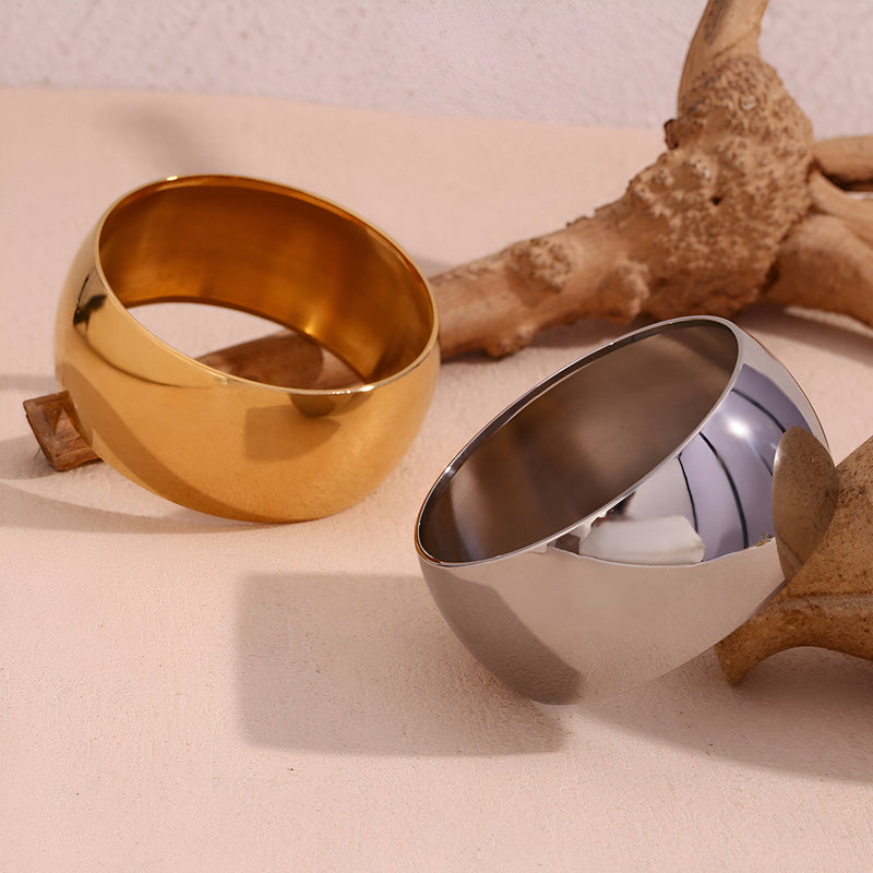 Bracelet manchette en acier inoxydable, design épuré, finition dorée et argentée, surface lisse et brillante.