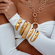 Bracelet manchette doré texturé en acier inoxydable, forme large et moderne, porté sur le poignet.