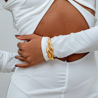 Bracelet manchette doré en acier inoxydable avec design fondu et forme organique, porté serré au poignet.