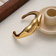 Bracelet manchette doré en acier inoxydable avec finition lisse et forme organique fluide.