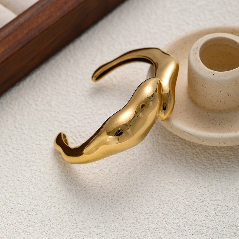 Bracelet manchette doré en acier inoxydable avec finition lisse et forme organique fluide.