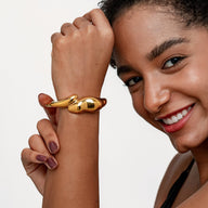 Bracelet manchette doré en acier inoxydable avec design organique fondu, forme incurvée et finition brillante.