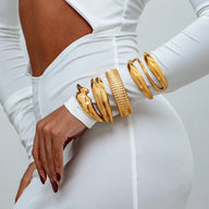 Bracelet manchette doré en acier inoxydable avec texture striée, forme large et design moderne porté au poignet.