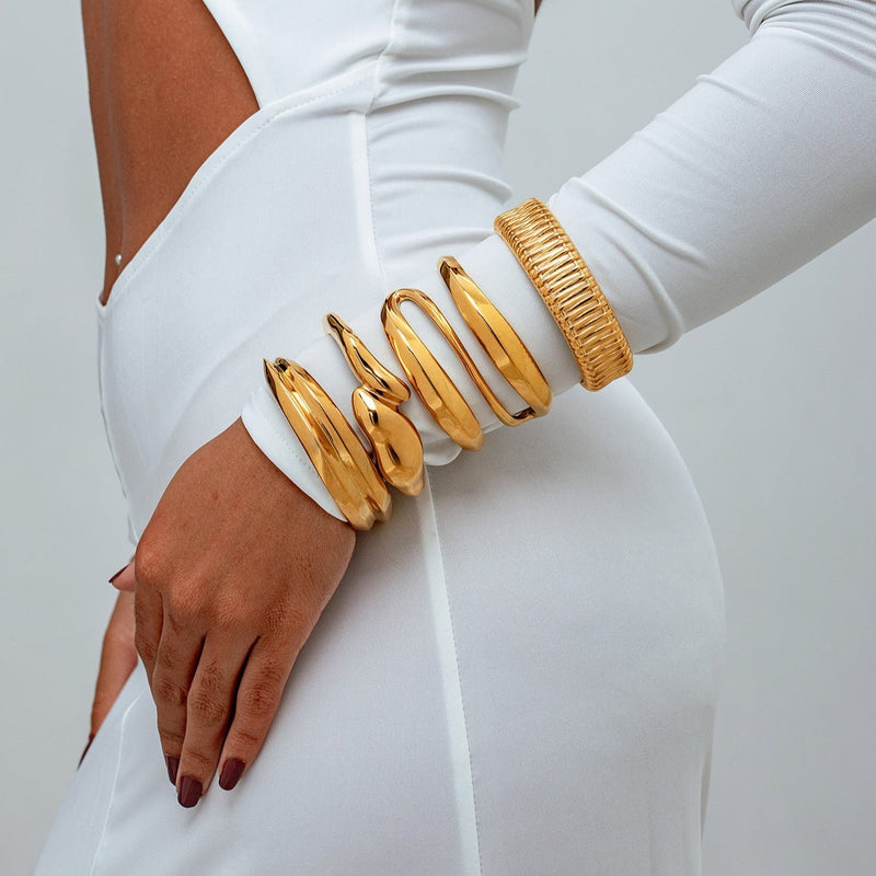 Bracelet manchette doré en acier inoxydable, large, avec texture rayée et design moderne sur poignet féminin.