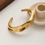 Bracelet manchette doré en acier inoxydable avec design fluide et forme incurvée épurée.