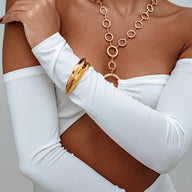 Bracelet manchette doré en acier inoxydable, design fluide et épuré, style Y2K, porté sur un bras avec un top blanc manches.