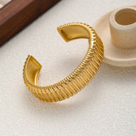 Bracelet manchette doré en acier inoxydable avec texture côtelée et finition brillante, design moderne.