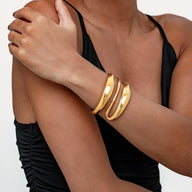 Bracelet manchette en acier inoxydable doré, design audacieux et sculpté avec surface lisse et formes courbes.