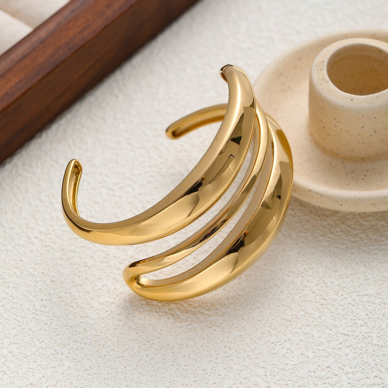 Bracelet manchette en acier inoxydable doré avec trois bandes courbées sculptées et finition lisse.