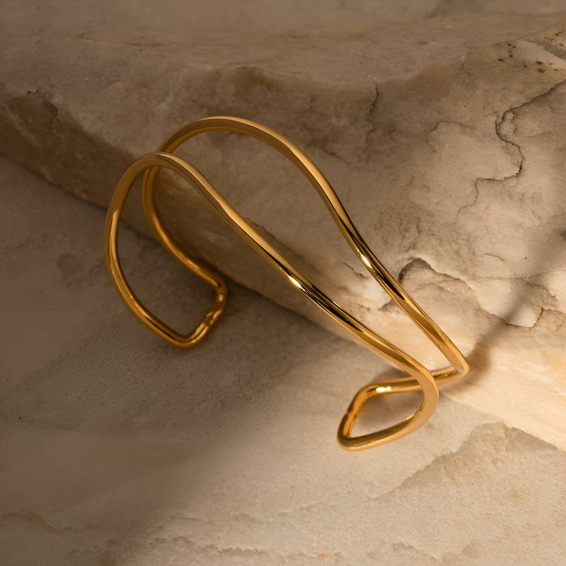 Bracelet manchette ouvert en titane plaqué or, design élégant et minimaliste avec courbes fluides.