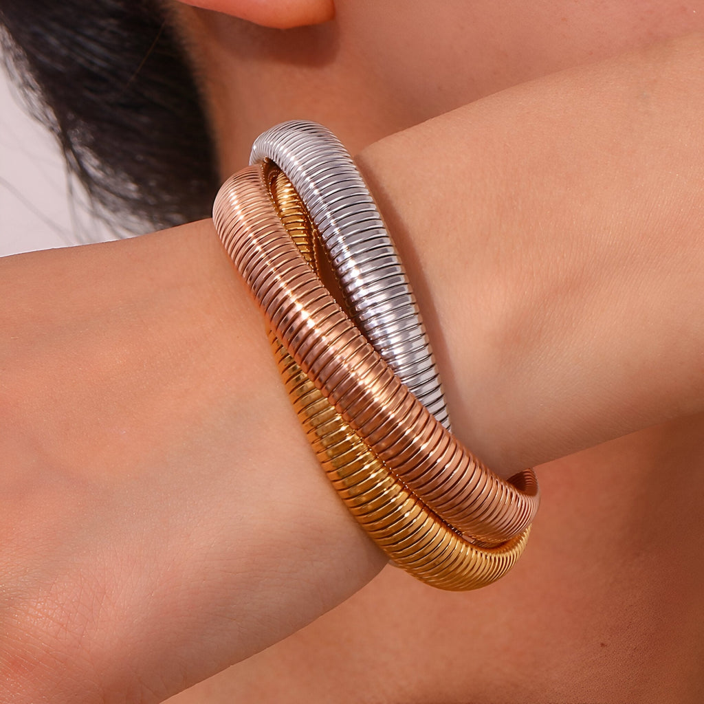 Trio de bracelets manchettes torsadés en argent, or rose et or jaune sur poignet féminin.
