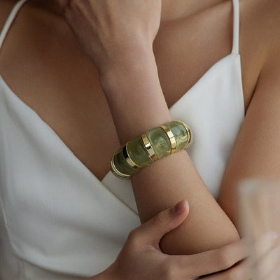 Bracelet manchette épais en acrylique vert transparent à reflets dorés porté sur poignet féminin.