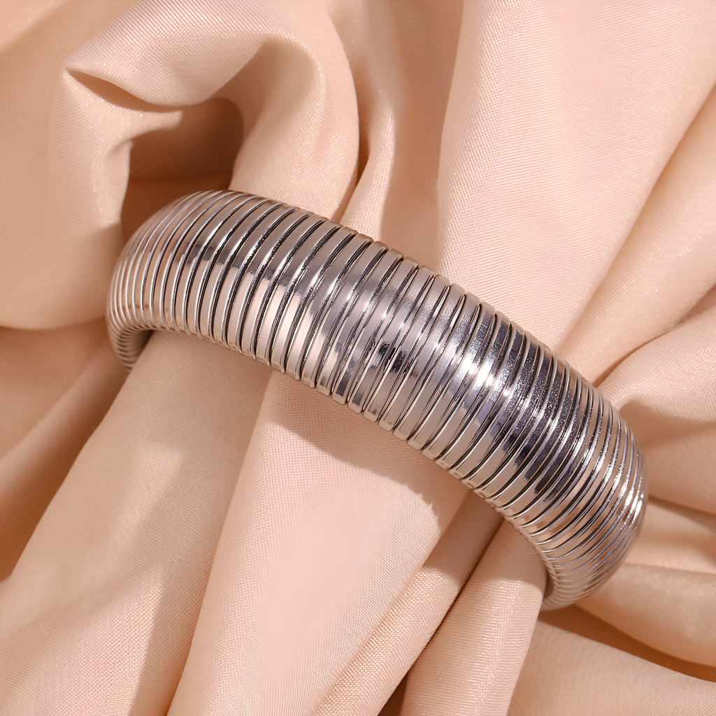 Bracelet manchette flexible en maille argentée modèle Aurélie posé sur tissu beige doux.