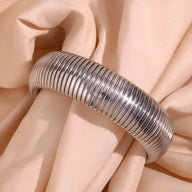 Bracelet manchette flexible en maille argentée modèle Aurélie posé sur tissu beige doux.